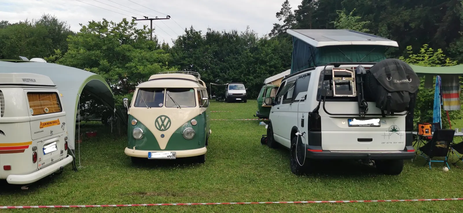 Camper und Vorzelte auf der Wiese vor dem Wald